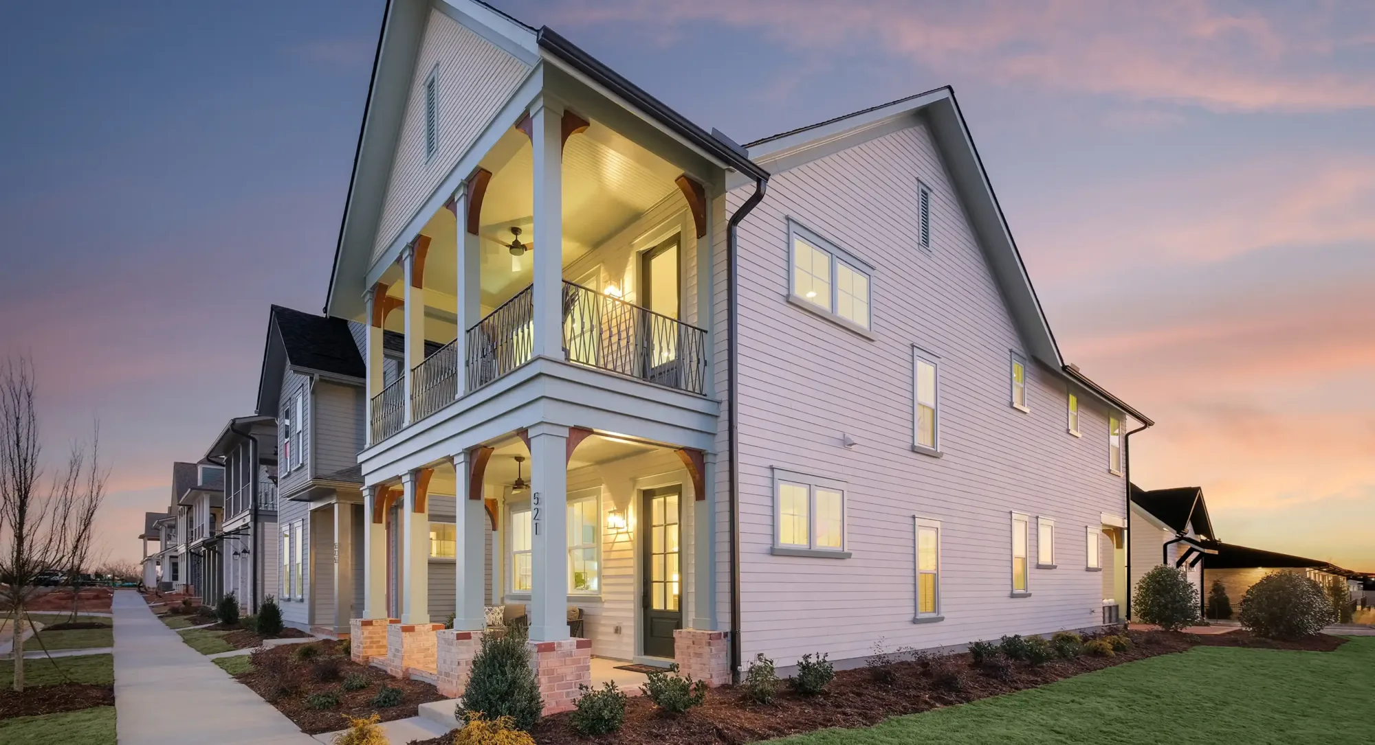 Exterior of large gray home in a row of houses at dusk with lit up windows